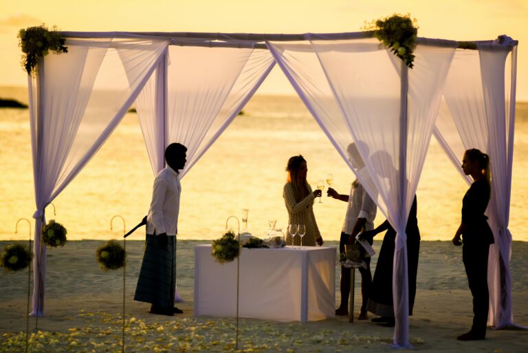 Elegant beach wedding ceremony setup with guests during a vibrant sunset on the waterfront.